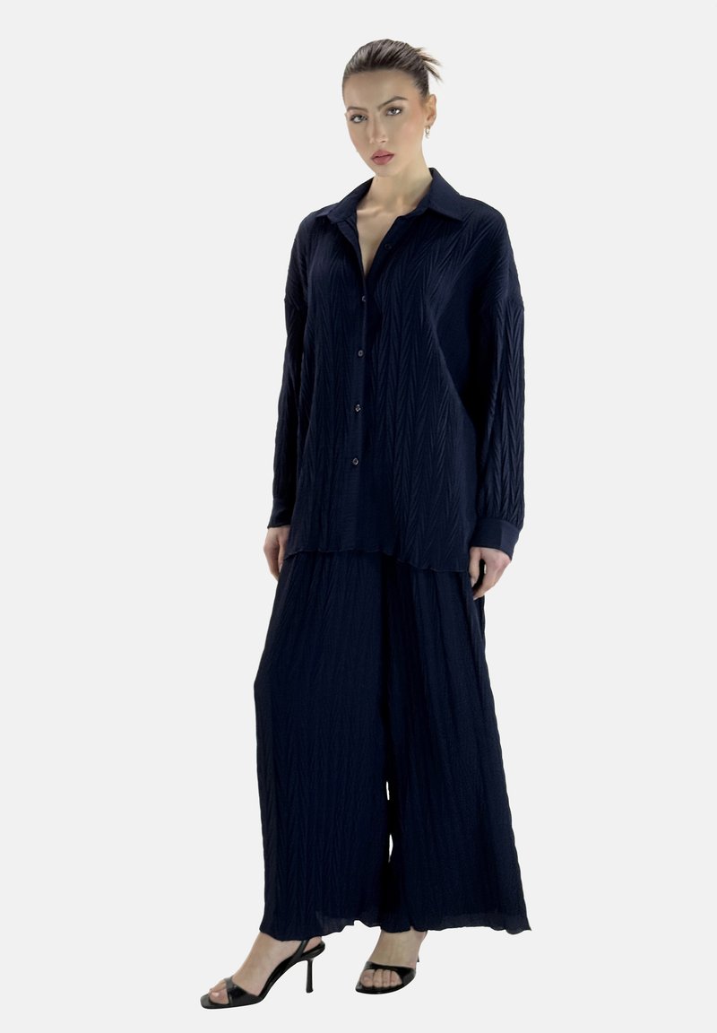 Conjunto de dos piezas en azul marino que incluye una camisa de botones, suelta y texturizada, y pantalones de pierna ancha, combinados con sandalias de tacón negras.