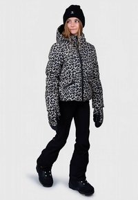 Leopárdmintás steppelt dzseki fekete részletekkel, vastag szigeteléssel és kapucnival, fekete nadrággal és hozzá illő kesztyűkkel párosítva.