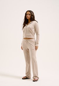Beige velours cropped hoodie met een rits aan de voorkant en zakken, gecombineerd met bijpassende licht taps toelopende broek met een trekkoord in de taille en zijnaad.