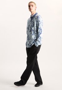 Ljusblå långärmad polo tröja med ett mörkblått ormtryck, kombinerad med svarta byxor och svarta halkfria skor.