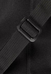 Schwarzer Stoffriemen mit einer strukturierten Oberfläche, ausgestattet mit einer quadratischen Kunststoffschnalle. Das Material wirkt strapazierfähig und robust.