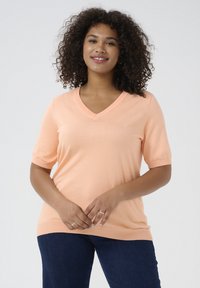 Perzikkleurig T-shirt met korte mouwen en V-hals, gemaakt van een zachte, lichte knit stof. Heeft een relaxed fit en ribbelstructuur aan de halslijn en mouwen.