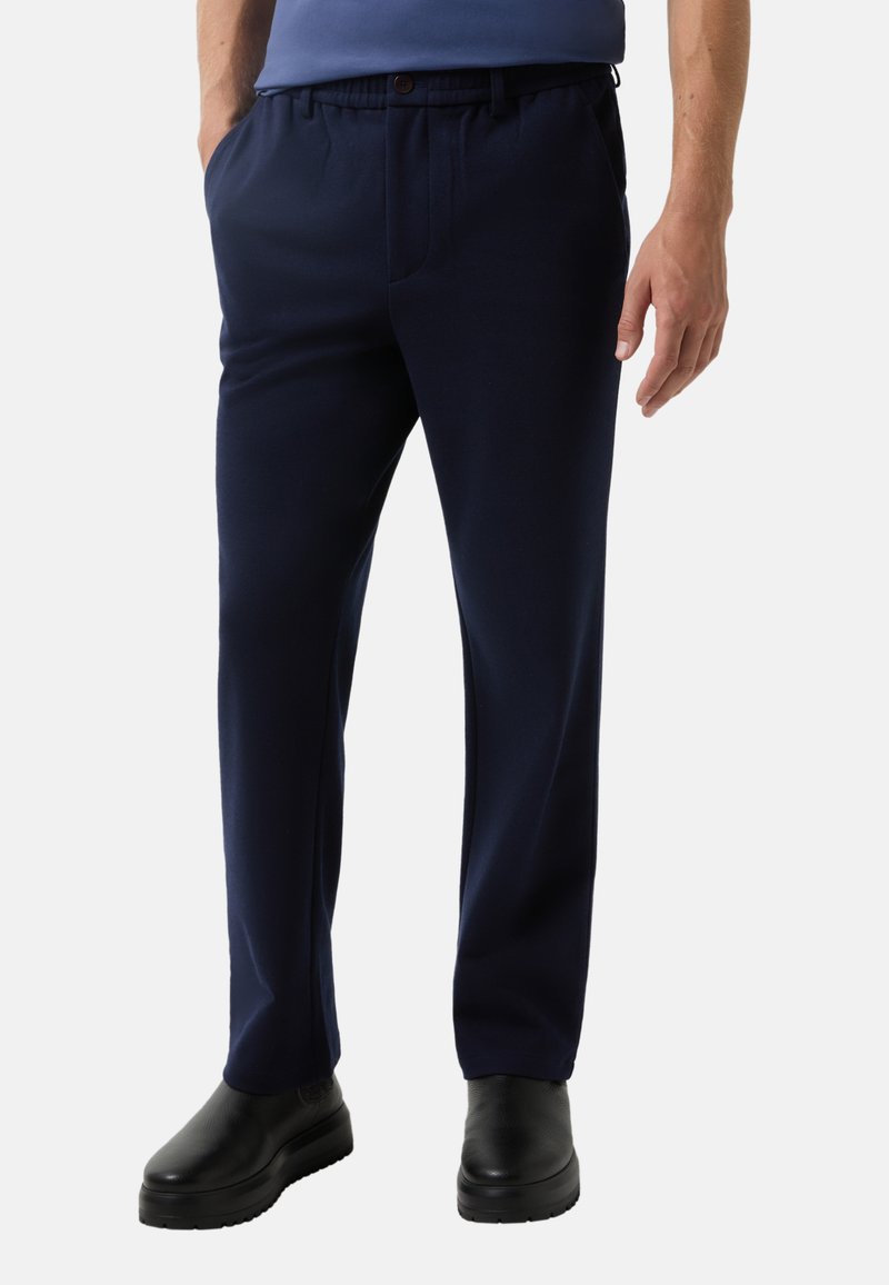 Marinblauwe broek met een losse pasvorm, elastische tailleband, voorplooien en zijzakken, gecombineerd met glanzende zwarte schoenen.