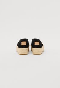 Čierne tkané slip-on topánky s jutovou platformou. Obsahujú hnedú koženú nášivku a textúrovaný zvršok. Plochá podrážka s zaoblenými hranami.