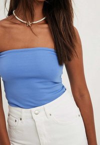 Blå axelbandslös topp i slät tyg, kombinerad med högmidjade vita denimshorts med metallknappar och fickor.