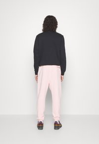 Czarna, skrócona bluza z długimi rękawami w połączeniu z różowymi dresami. Dresy mają luźny krój i elastyczne ściągacze; czarne sneakersy dopełniają stylizację.