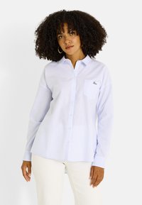 Camisa azul claro a rayas con botones, hecha de algodón, con mangas largas, cuello, un bolsillo en el pecho izquierdo y detalle bordado.