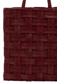 Tkaná kožená taška v tmavě burgundské barvě. Design obsahuje strukturovaný, křížový vzor s plochými popruhy a pevnými okraji.