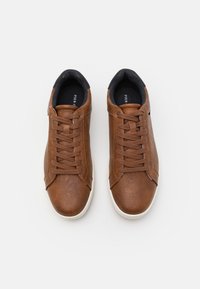 Baskets en cuir marron avec une finition texturée, bout rond, lacets plats et semelle extérieure en caoutchouc blanc. Doublure intérieure noire, détail de marque minimal.