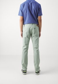 Pantalones verde claro de corte recto, con bolsillos laterales y traseros. Combinados con una camisa azul de manga corta y zapatos negros con detalles en neón.