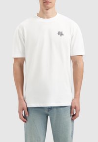 Witte katoen T-shirt met korte mouwen, ronde hals en een zwart grafisch print op de linkerborst. Standaard pasvorm en soepele textuur.