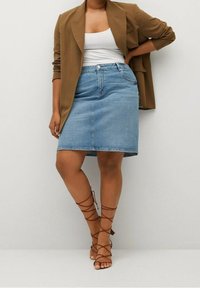 Jupe crayon en denim bleu clair, mi-longue avec une fente à l'avant, associée à un blazer marron et des sandales à talons marron. Un simple haut blanc en dessous.