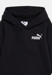 Μαύρο φούτερ Puma με μπροστινή τσέπη καγκουρό και λευκό λογότυπο Puma στο στήθος, κοντινή άποψη του πάνω μέρους του ενδύματος.