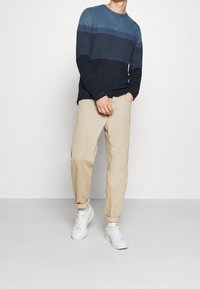 Stickad marinblå och blå randig tröja, beige byxor och vita sneakers. Avslappnad passform, långa ärmar och rund halsringning. Slät textur.