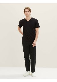 Tricou negru din bumbac cu decolteu în V, asortat cu pantaloni negri și adidași albi, având un design simplu și mâneci scurte.