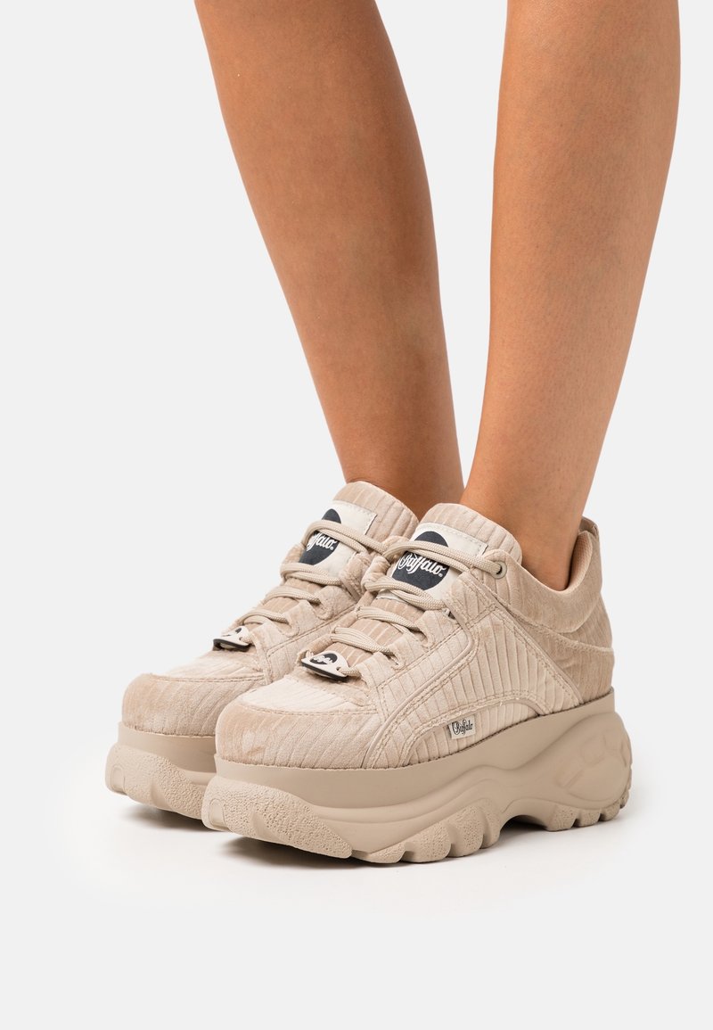 Baskets à plateforme beige avec texture côtelée et semelles épaisses portées sur des jambes nues sur un fond clair uni.