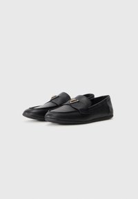 Black loafers made of textured leather, featuring a smooth toe design. Accented with a triangular metal detail on the front.