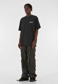 Tricou negru supradimensionat cu mâneci scurte și text alb pe piept, asortat cu pantaloni cargo închisi la culoare, cu multiple buzunare și o croială lejeră.