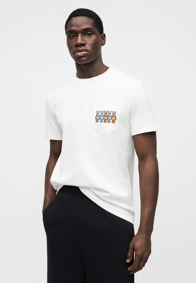 Λευκό βαμβακερό μπλουζάκι με τσέπη στο στήθος που έχει πολύχρωμο κέντημα με σχέδιο κουνελιού. Το μπλουζάκι έχει άνετη εφαρμογή και στρογγυλή λαιμόκοψη.