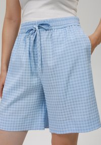 Světle modré kostkované šortky z měkké tkaniny. Elastický pas s nastavitelným šňůrkovým uzávěrem a bočními kapsami. Pohodlný, volný střih.