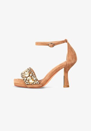 Sandalias de tacón alto de ante color marrón con tira en el tobillo, que presentan una tira frontal decorada con grandes piedras transparentes y ámbar.