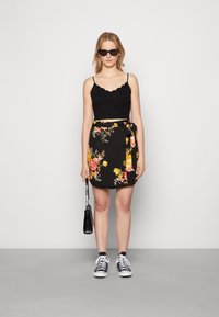 Saia rodada preta com flores amarelas e rosas, combinada com um top cropped ajustado preto e ténis pretos. Acessorizada com uma mala preta.