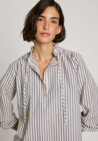 Button-up skjorte med en bølget krave, prydet med lodrette blå og beige striber. Lavet af blødt stof med oprullede ærmer og en afslappet pasform.