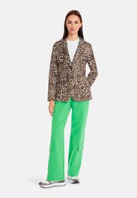 Leopard print blazer with a tailored design, paired with green wide-leg pants and patterned sneakers. Smooth fabric with structured fit.