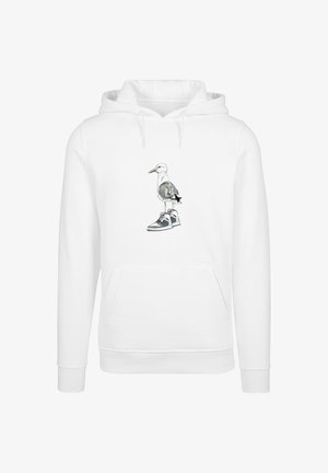 Valkoinen huppari, jossa on graafinen kuva lokista, joka seisoo lenkkarilla. Kengässä on harmaata ja mustaa yksityiskohtaa.