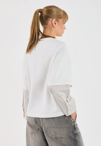 Witte oversized t-shirt met korte mouwen, gelaagd over een gestreept shirt met lange mouwen. Lichtgrijze high-waisted jeans met zakken.