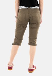 Pantalons capri kaki avec poignets retroussés, dotés de deux poches arrière et d'une ceinture à motifs. Portés avec des baskets rouges et crème.