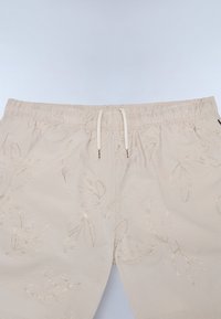 Beige shorts van een textuurstof, met een subtiel bladpatroon in goud, elastische tailleband en een trekkoordsluiting.