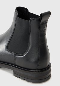 Botín Chelsea de cuero negro con textura suave, paneles laterales elásticos y una suela de goma resistente con un tacón ligeramente elevado.