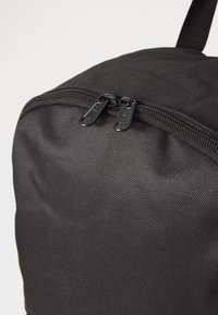 Schwarze Stofftasche mit runder Form, ausgestattet mit einem doppelten Reißverschluss und strukturiertem Oberflächenmaterial. Minimalistisches Design ohne sichtbare Logos.