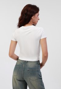 Hvid kortærmet tætsiddende t-shirt med en glat tekstur, parret med højtaljede falmede grønne jeans med to baglommer.