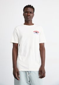 White cotton T-shirt with short sleeves, featuring a multicolored "Volcom Store" logo on the chest, paired with light blue denim shorts.