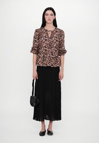 Leopard print blouse with a peplum waist, black pleated skirt, and black handbag. Model wears black flats and has long straight hair.