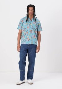 Short-sleeved, light blue shirt with multicolored floral and leaf patterns; paired with loose-fitting blue jeans and white sneakers.