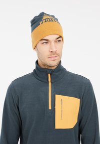Donkerblauwe fleece pullover met een rits bij de hals, oranje zak en logo. Het model draagt een bijpassende donkerblauwe en oranje muts.