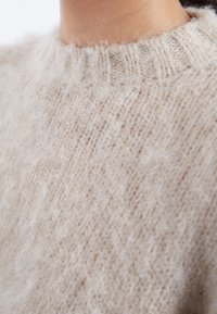 Beige knitted sweater with a high, ribbed neckline. Soft, fluffy texture with a subtle pattern, emphasizing warmth and comfort.