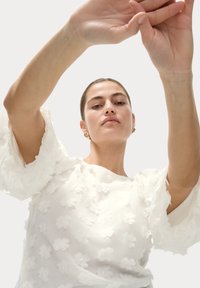 Witte blouse met geplooide mouwen, versierd met bloemapplicaties. Zachte stof, met een rechte halslijn en een subtiele glans.