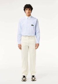Camisa de botones a rayas celeste con cuello blanco, combinada con pantalones color crema y zapatos con un patrón en blanco y negro.