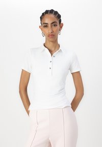 Weißes Poloshirt mit kragenloser Halslinie, drei Knopfverschluss und gerafften Seitenakzenten, kombiniert mit hellrosa maßgeschneiderten Hosen.