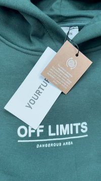 Zelena kapuljača s mekom teksturom, s bijelim ispisanim tekstom "OFF LIMITS" i "DANGEROUS AREA." Uključuje dvije oznake, jednu s informacijama o održavanju.
