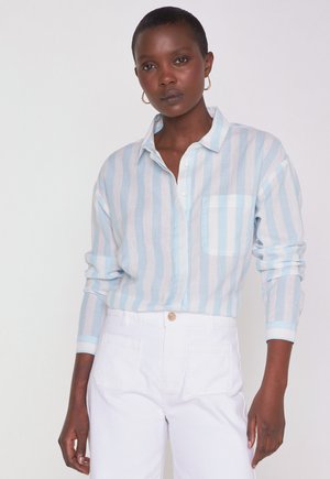 Light blue and white striped shirt with a button-up collar, single chest pocket, and long sleeves, paired with white pants.