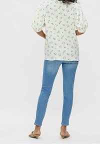 Blusa leggera gialla con motivo floreale e maniche a sbuffo, abbinata a jeans in denim blu aderenti e sandali beige senza chiusura. Look semplice e casual.