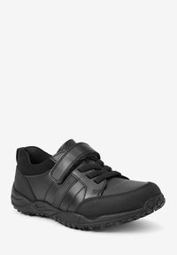 Chaussure de sport noire alliant cuir lisse et tissu texturé, avec une bande Velcro et une semelle en caoutchouc dotée d'un motif de traction.