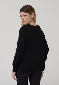 Maglione nero a maniche lunghe realizzato in tessuto morbido, con una vestibilità comoda, scollo a rotondo e polsini a costine. Design minimalista senza motivi.