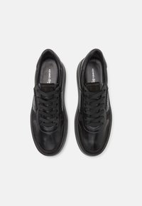 Pár černých kožených tenisek se šňůrkami, uvnitř značky "Kennel & Schmenger" a na jazyku "1916", zobrazených z vrchu na bílém pozadí.