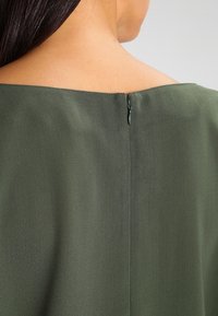 Robe en tissu vert avec un décolleté carré, texture lisse et une fermeture éclair discrète à l'arrière. Design simple et élégant.